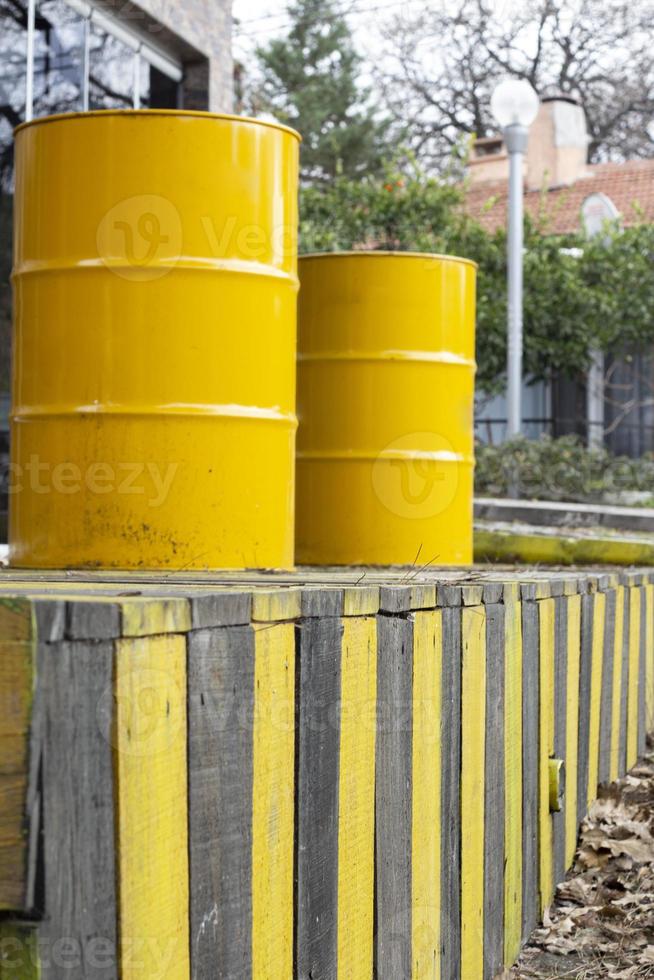 amarillo barriles en un de madera cerca en el calle. amarillo barriles de petróleo en el antecedentes de un fila de amarillo y negro cercas foto