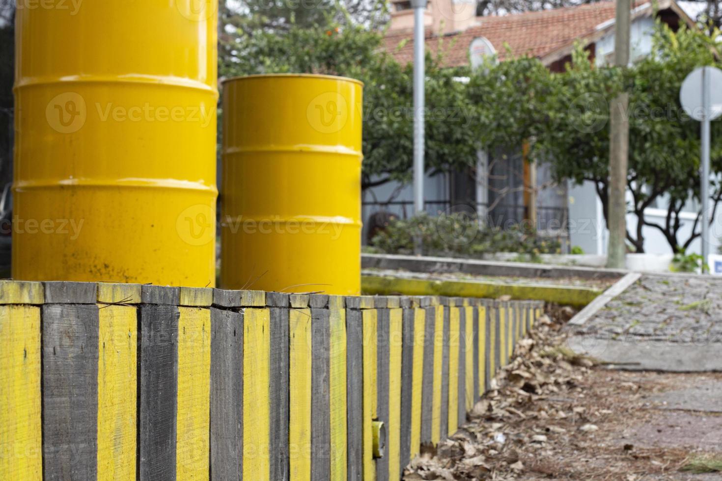 Yellow barrels on a wooden fence in the street. Yellow barrels of oil on the background of a row of yellow and black fences. photo