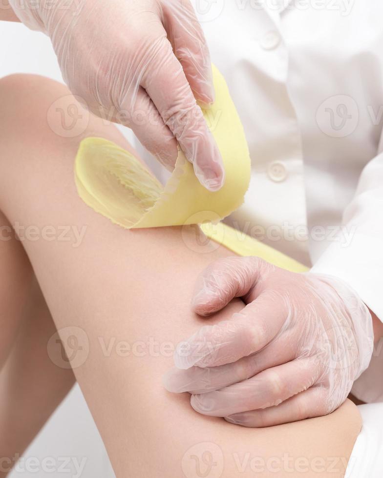 Closeup of beautician hands doing depilation to woman legs with green hot wax in beauty salon photo