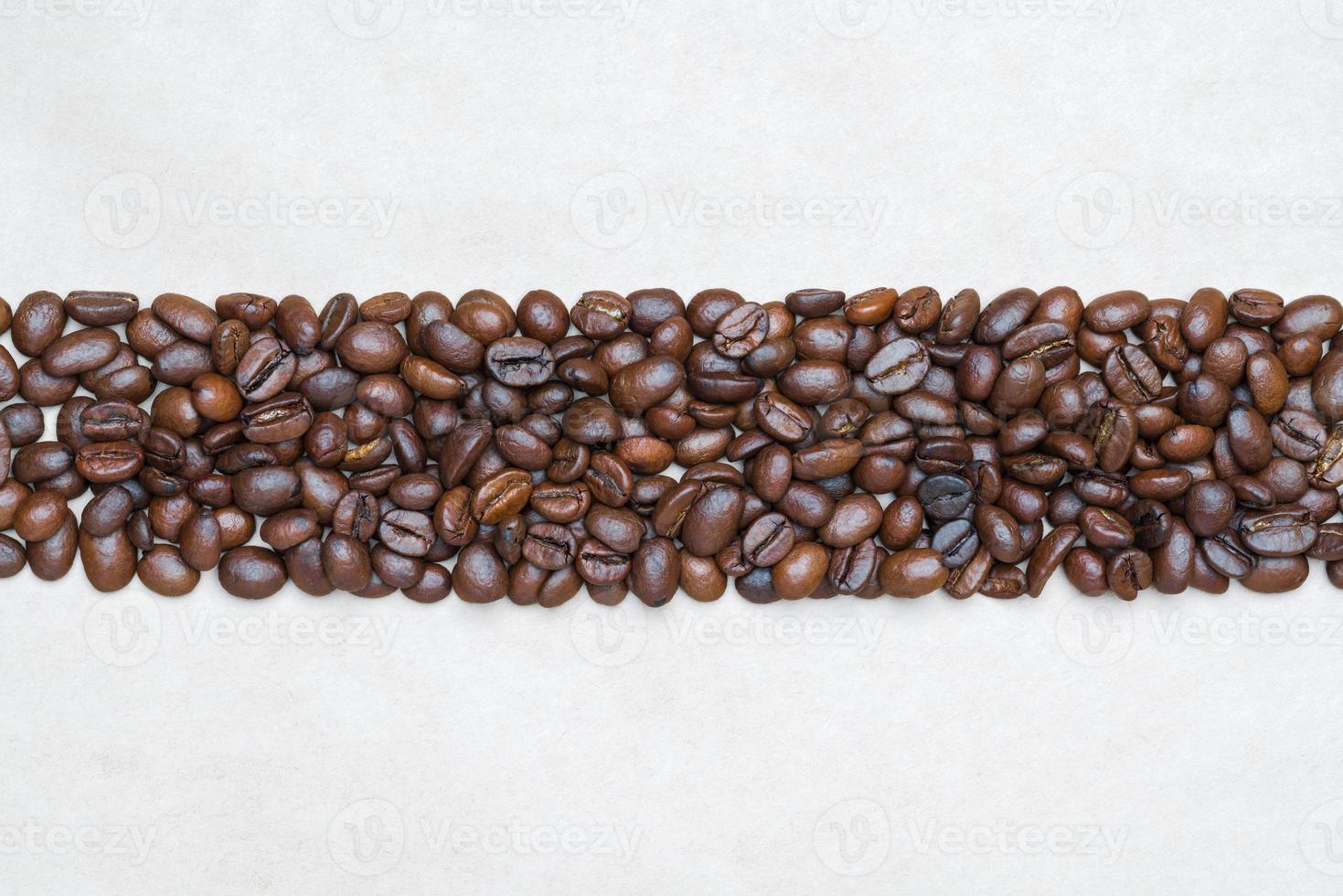 Brown coffee beans on background of recycled eco-friendly paper. Central horizontal location objects, copy space at top and bottom. Flat lay, close-up view of still life photo