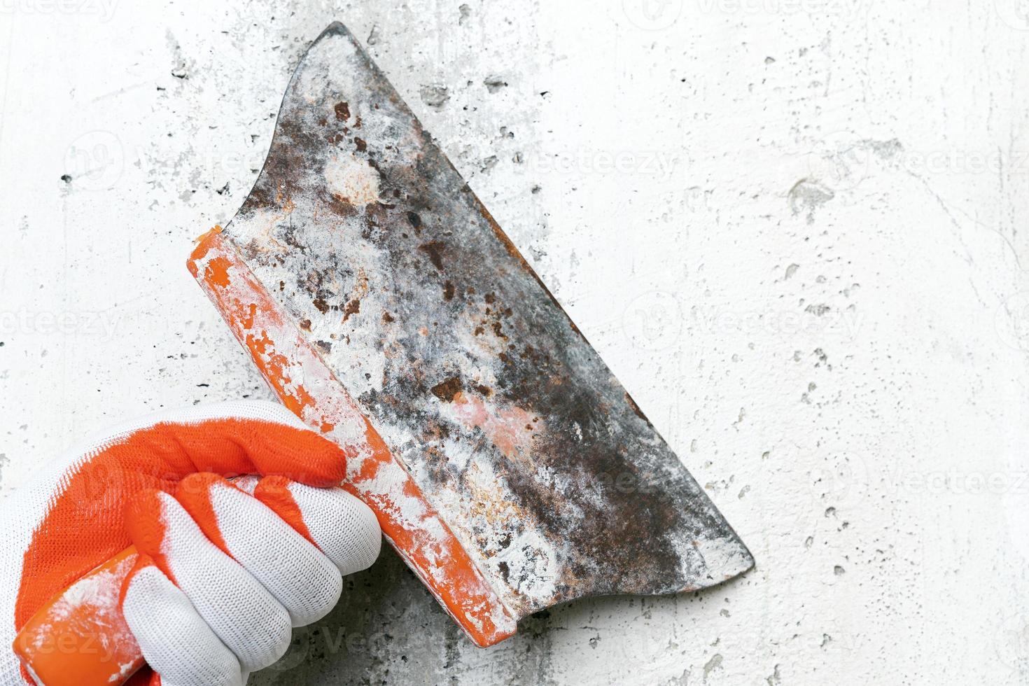 Hand of plasterer holds an old putty knife and scrapes concrete interior wall, removes old plaster photo