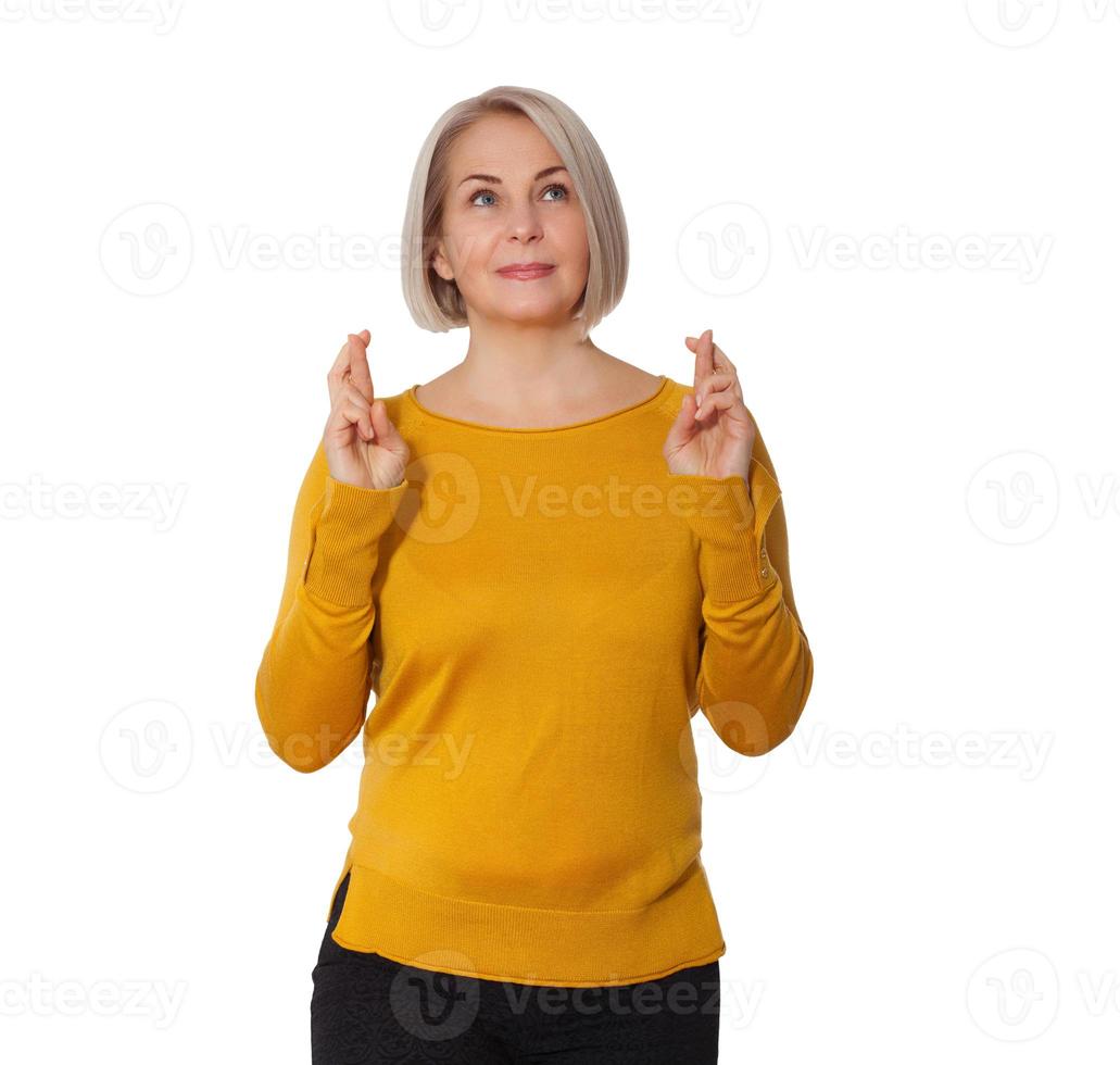 Attractive Middle Aged Woman crosses fingers making wish expressing joyful emotions. Woman in bright clothes posing in studio on white background photo