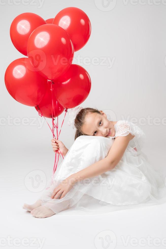 Romantic girl holding lot of red balloons, put head on knees, sitting on white background photo