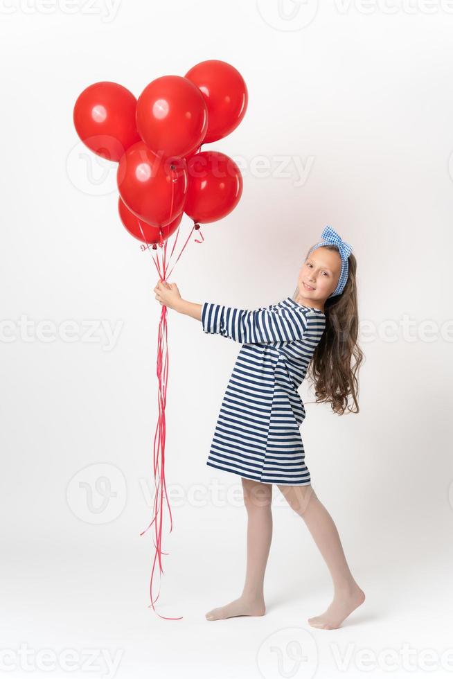 Shy girl 10 years old holding red balloons in hands looking at camera. Full length white background photo