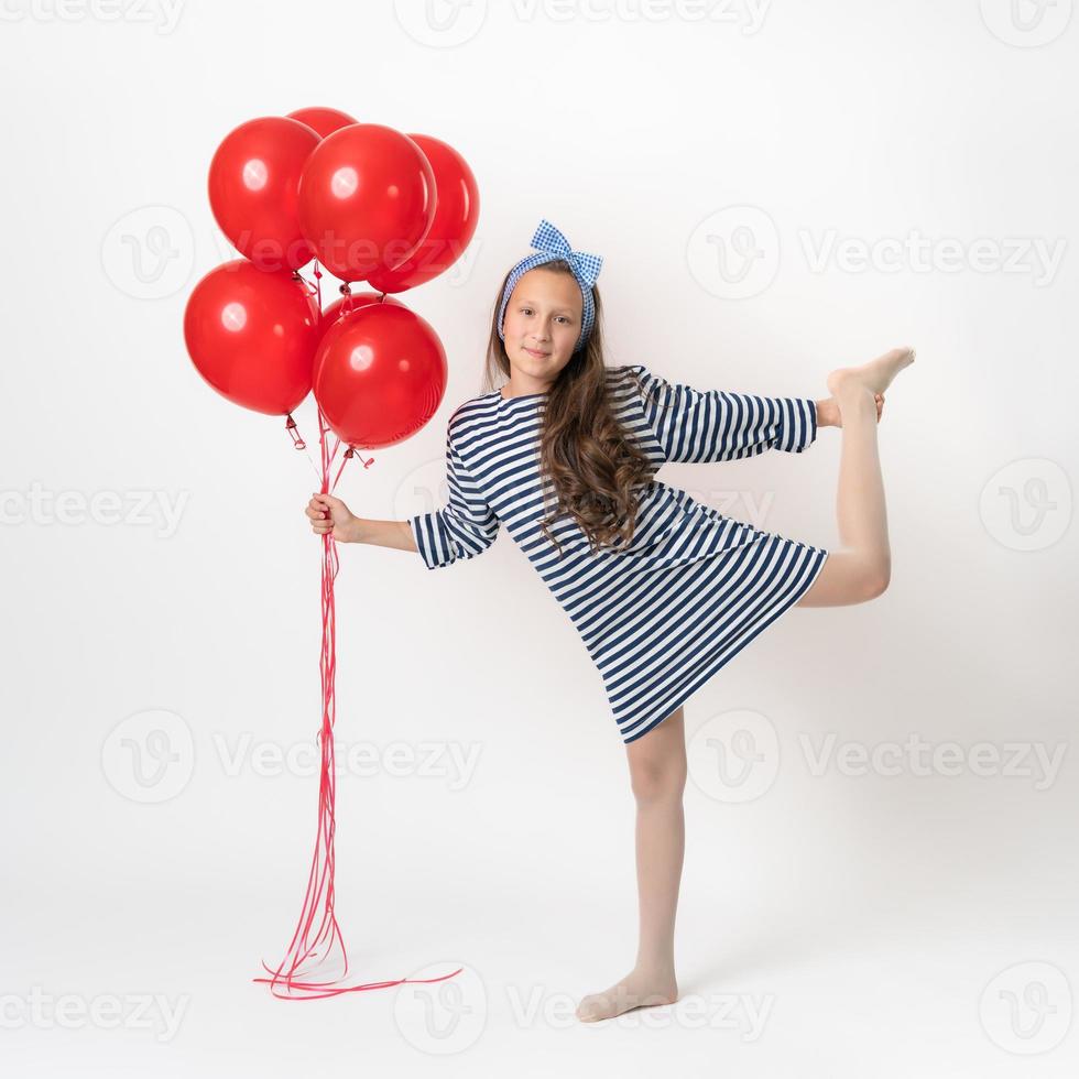 Active girl posing, holding bunch of red balloons in hand, standing on one leg on white background photo