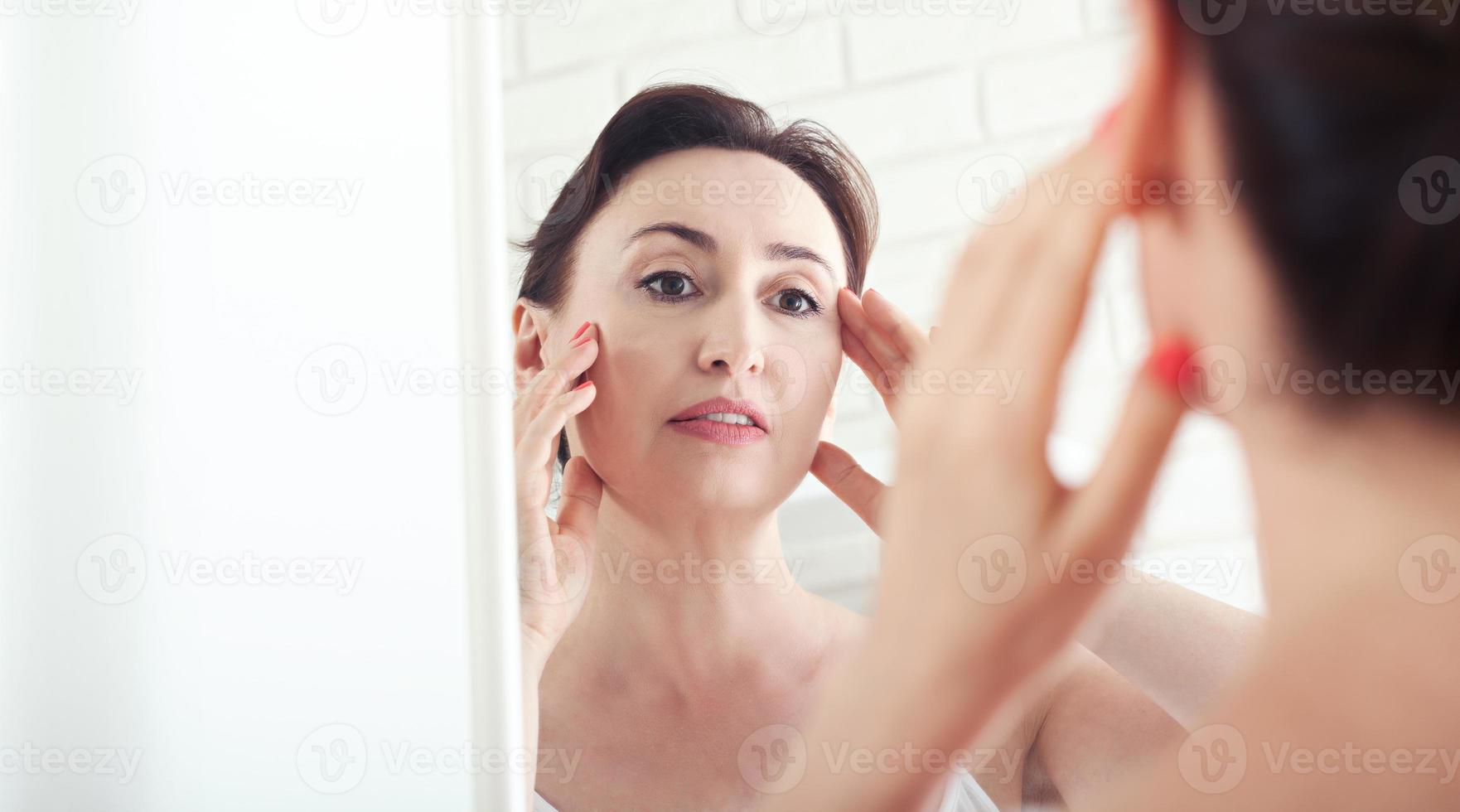 Woman looking at wrinkles in mirror. Plastic surgery and collagen injections. Makeup. Macro face. Selective focus photo