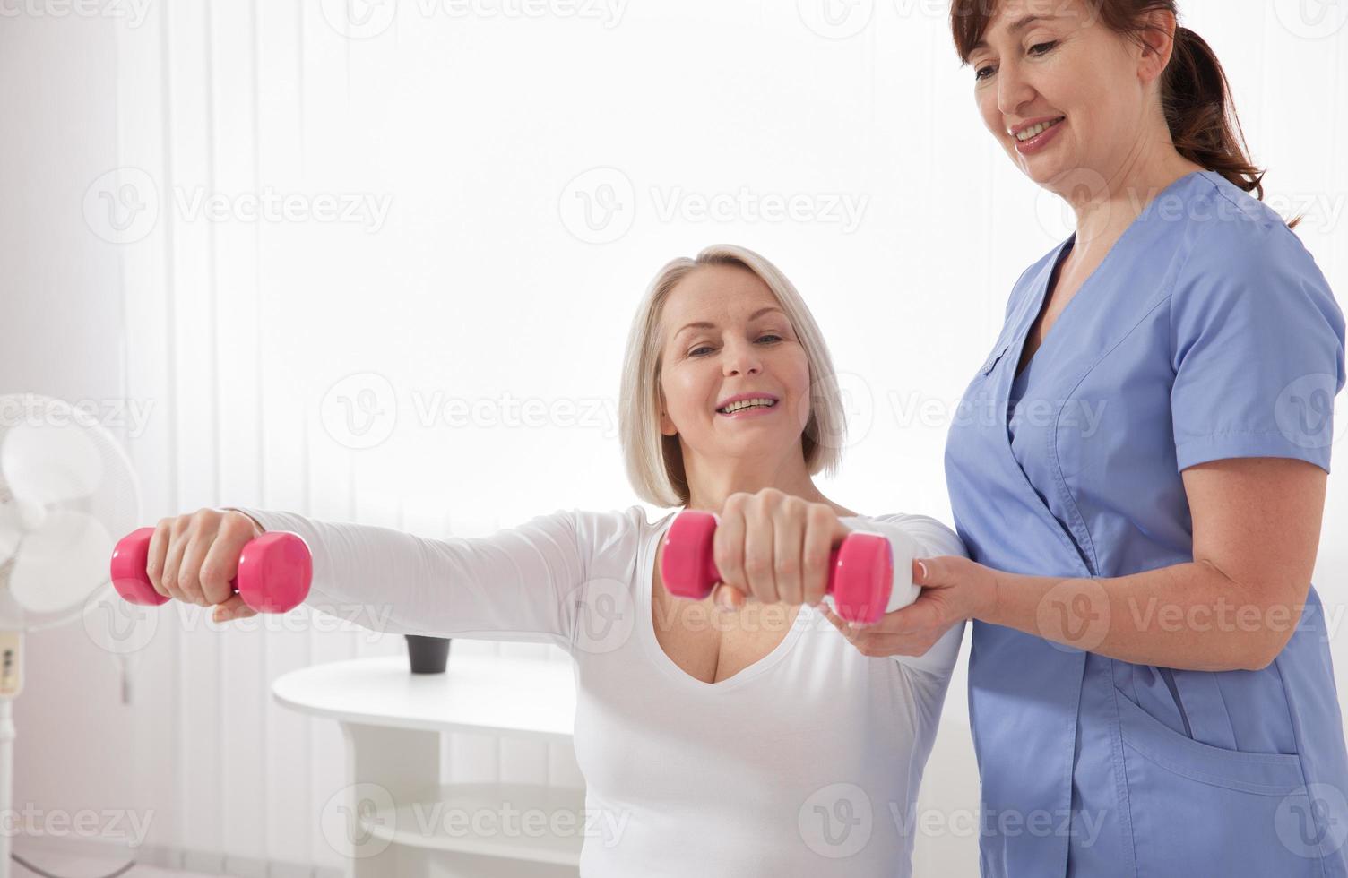 Modern rehabilitation physiotherapy. Physiotherapist helps an middle aged woman recover from an injury through exercise with dumbbells. photo