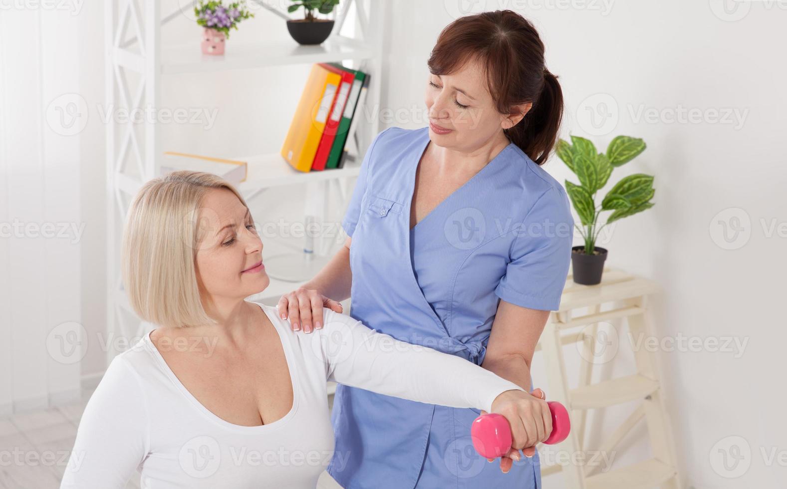 Modern rehabilitation physiotherapy. Physiotherapist helps an middle aged woman recover from an injury through exercise with dumbbells. photo