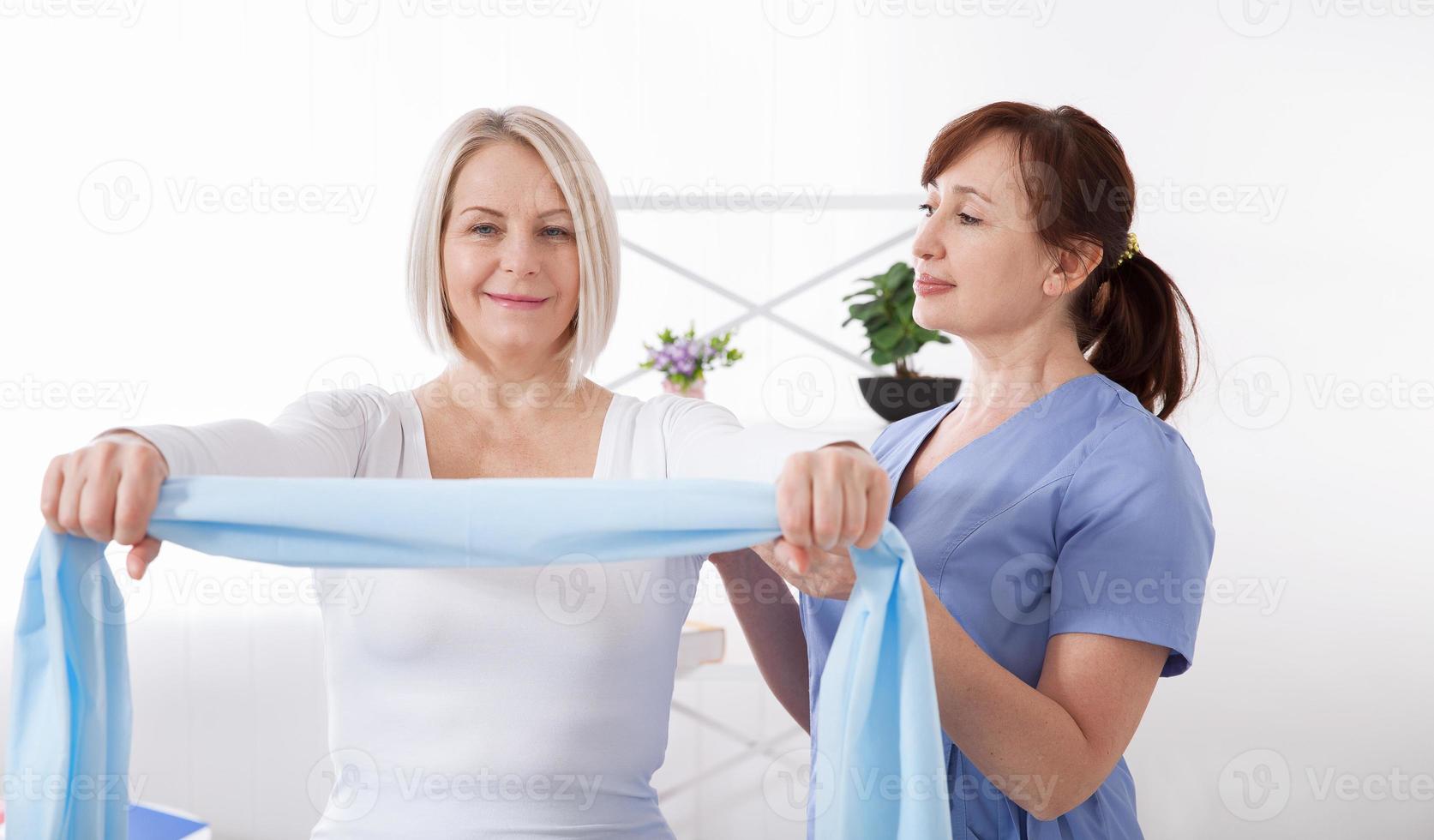 fisioterapeuta y mujer sentada en una cama haciendo ejercicio con una cinta de goma foto