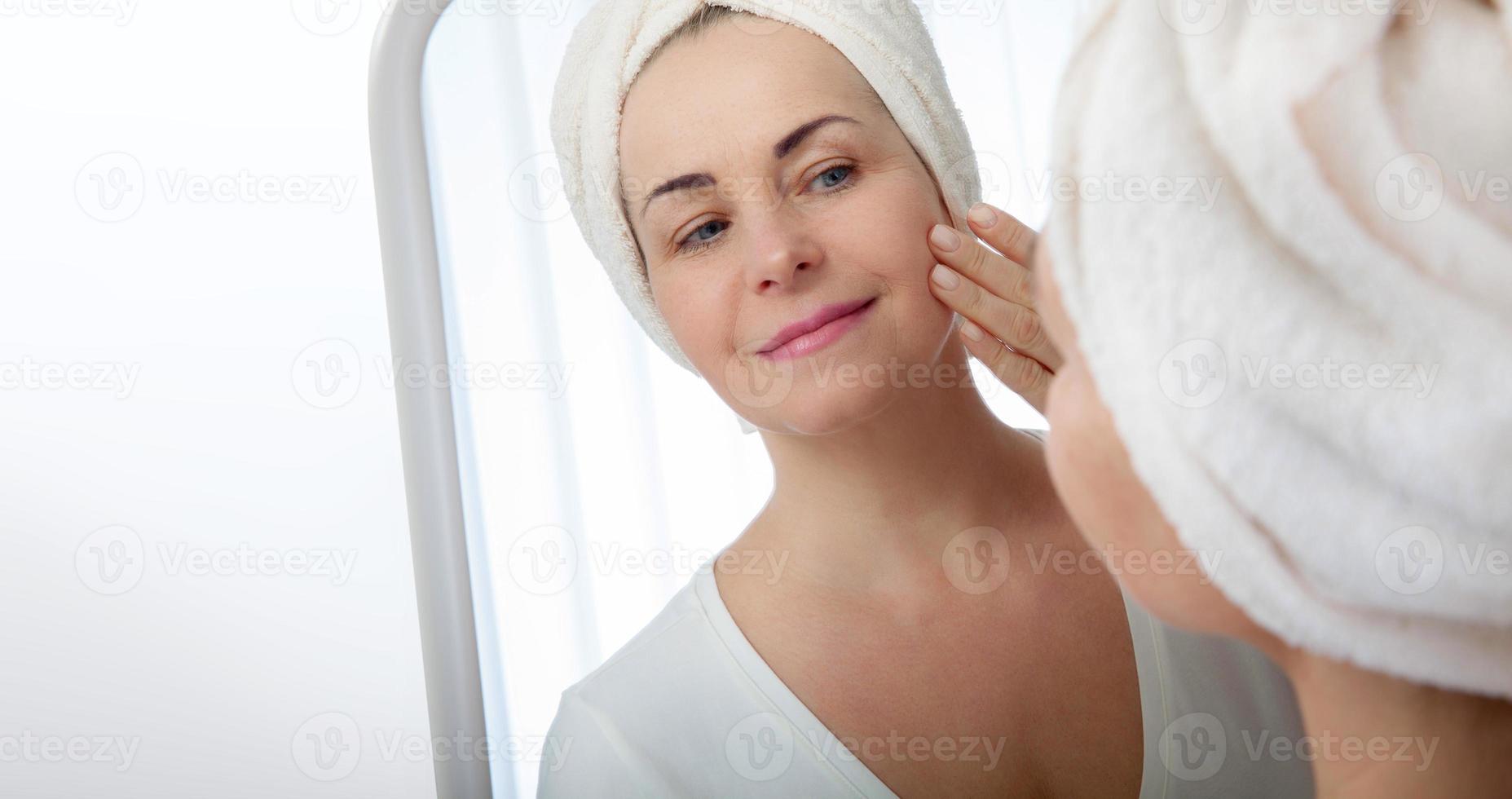 Forty years old woman looking at wrinkles in mirror. Plastic surgery and collagen injections. Selective focus on the face. photo