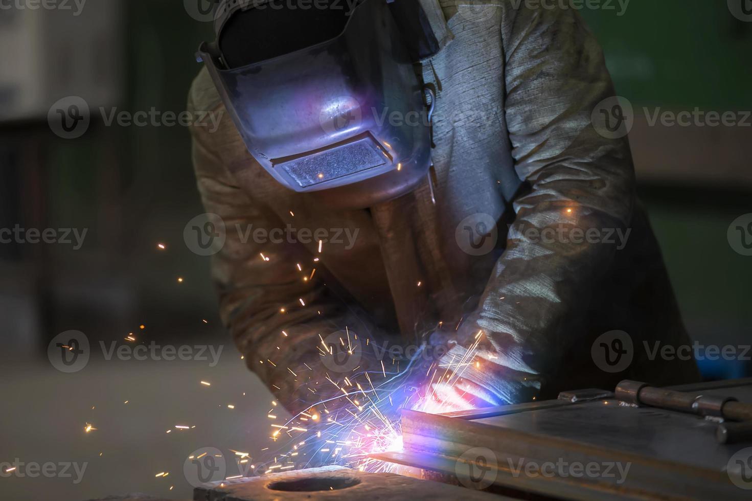 soldador a trabajar. hombre en un protector mascarilla. el soldador hace costuras en el metal. chispas y fumar cuando soldadura. foto