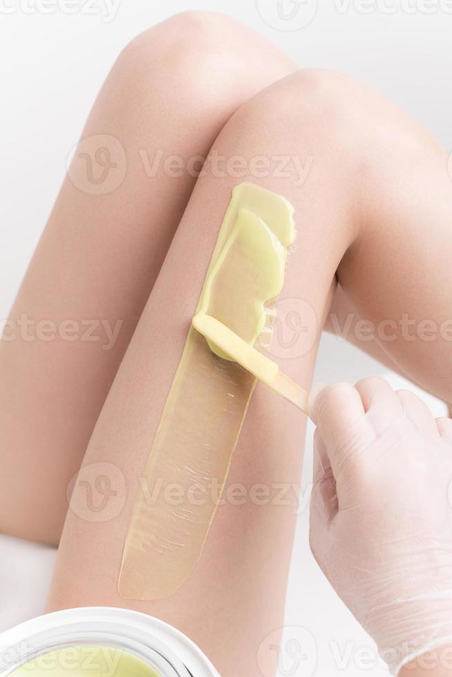 aplicando caliente cera en Delgado mujer pierna utilizando espátula. profesional depilación, depilación en belleza salón foto