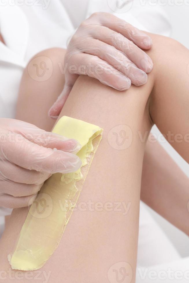 Closeup view of cosmetologist removing hair on female leg using hot wax in professional beauty salon photo