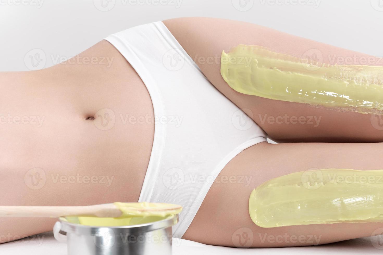 Legs of slim woman while she lying down on couch during depilation process with green hot wax photo