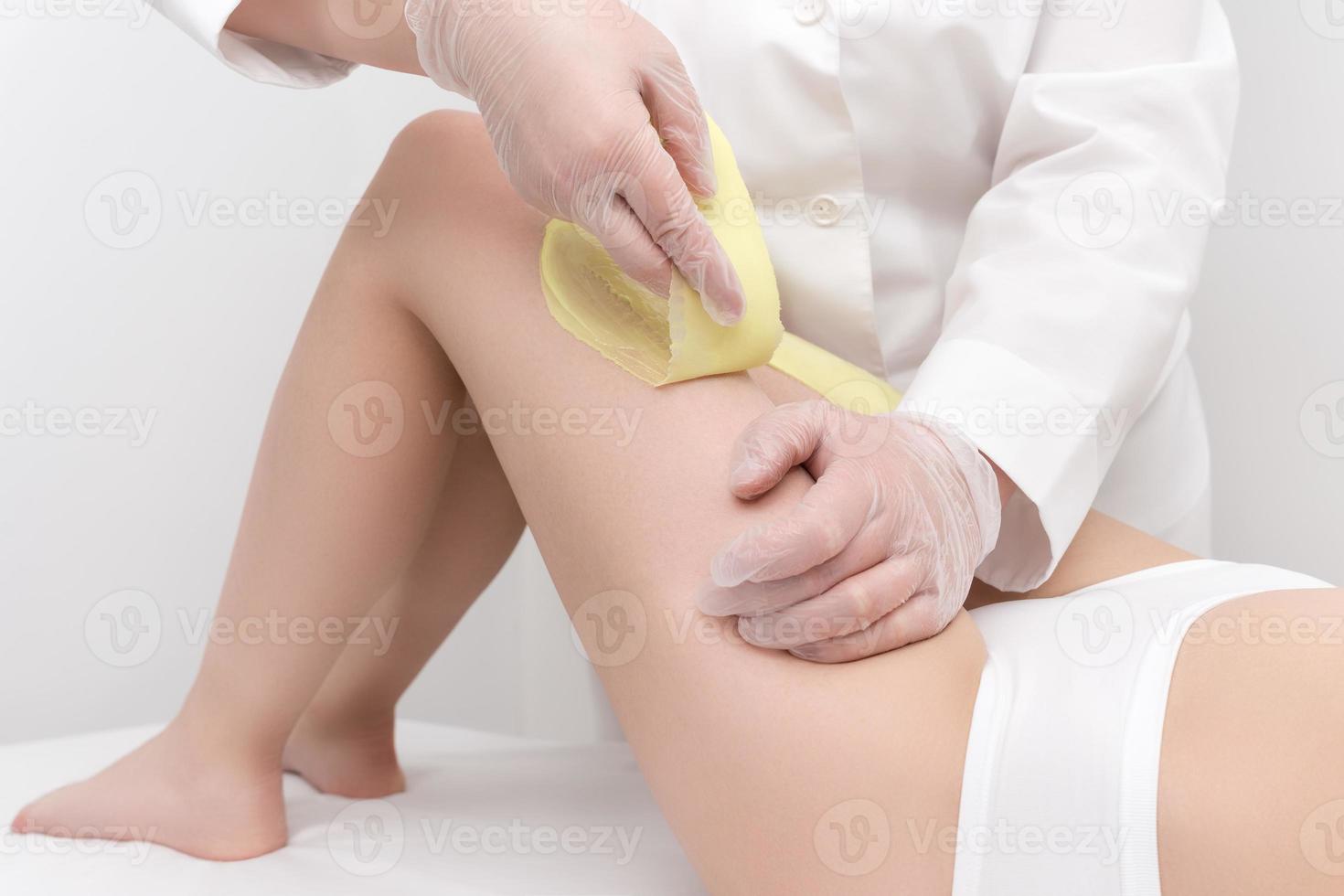 Cosmetologist hands in gloves removing hair on women leg. Depilation procedure photo