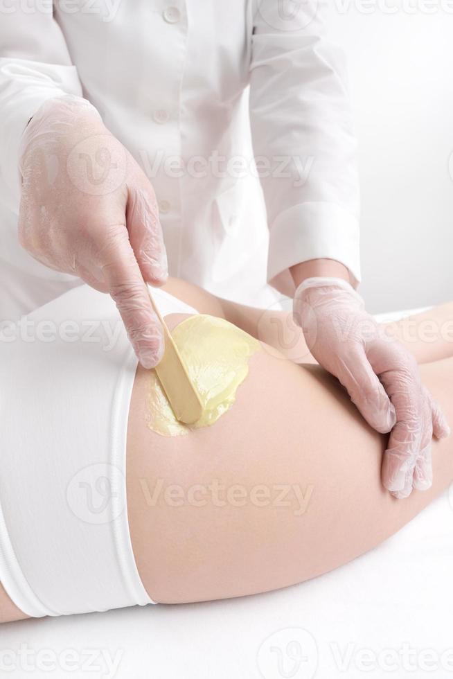 Master applying green hot wax on woman buttocks using spatula. Depilation with wax in beauty salon photo