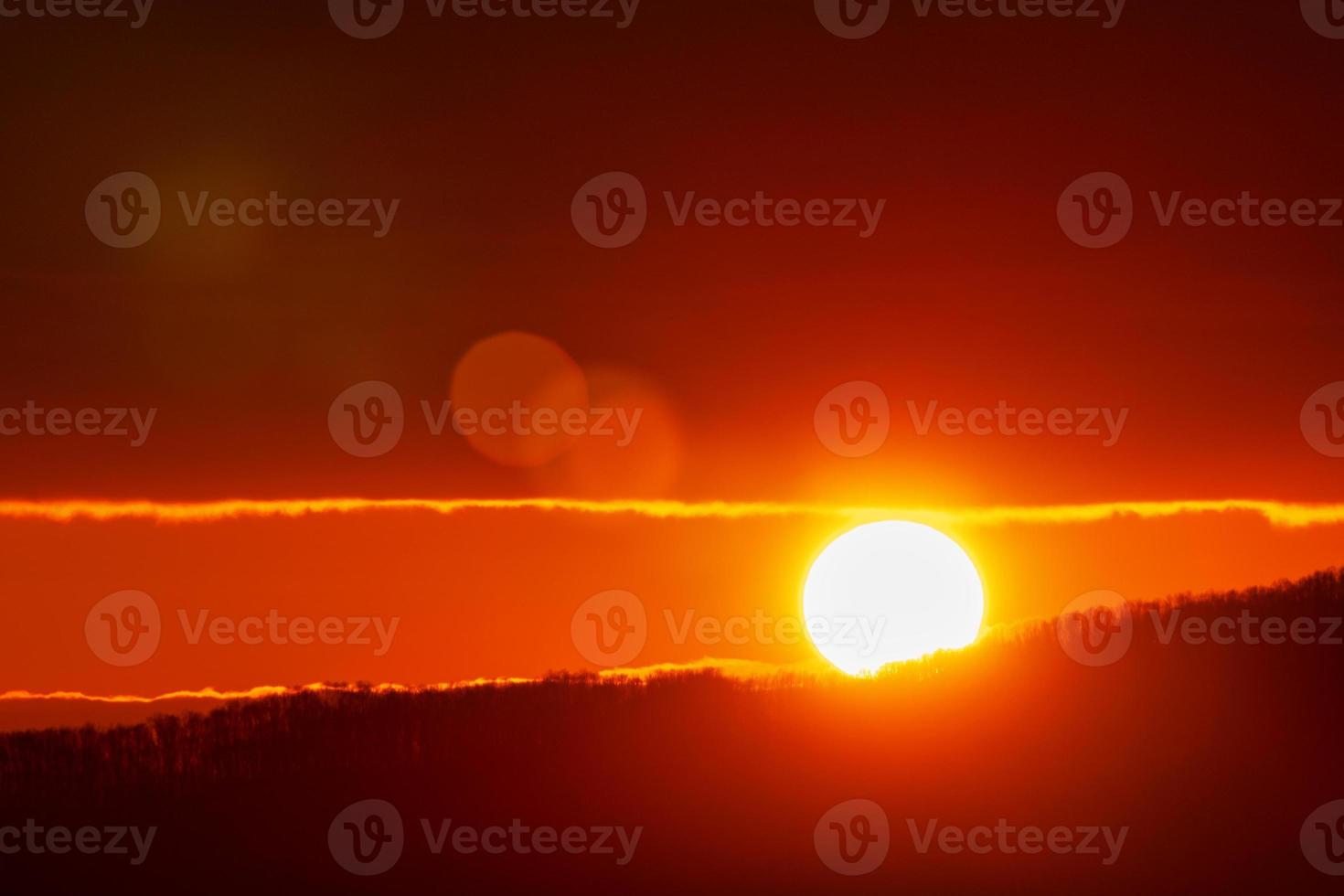 Beautiful sunrise in mountains, red sun disk rises from tops of mountain range. Natural lens flare in sky photo