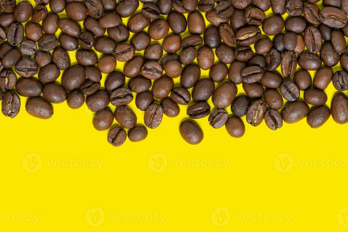 Brown coffee beans on yellow background. Top horizontal location objects, copy space for text at bottom. Flat lay, close-up view of coffee still life photo