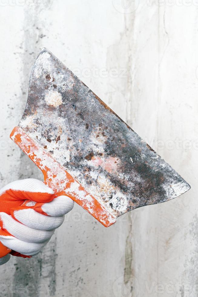 Plasterer holds an old special scraper in his hand on background of gray concrete wall photo