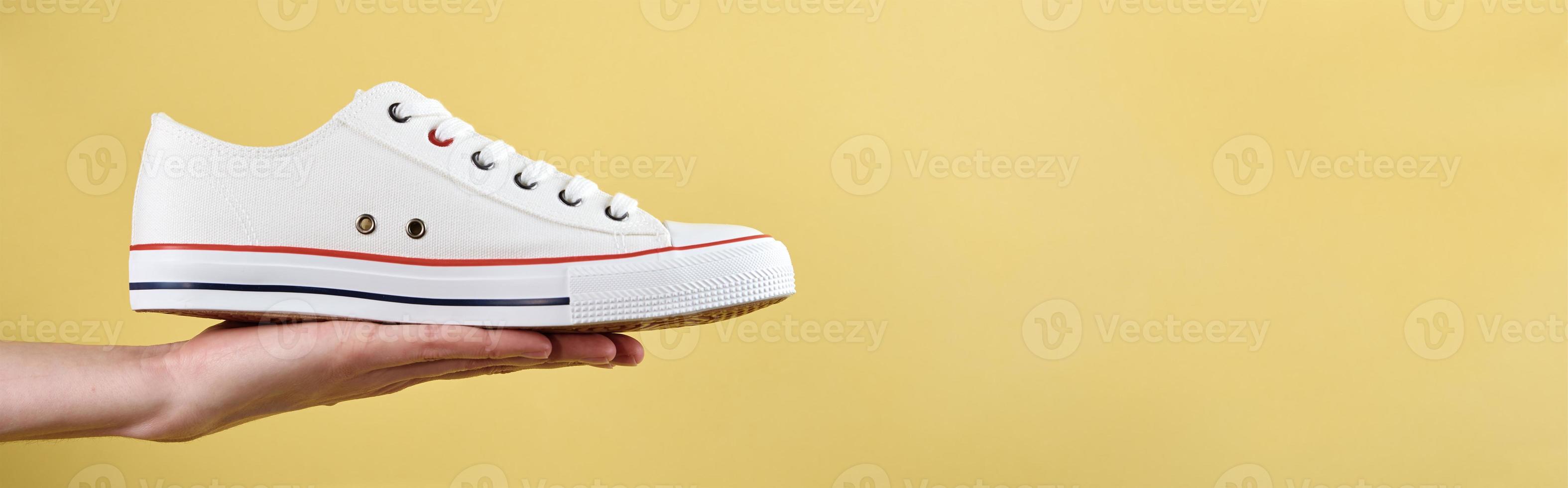 Woman hand hold casual shoe on yellow background photo