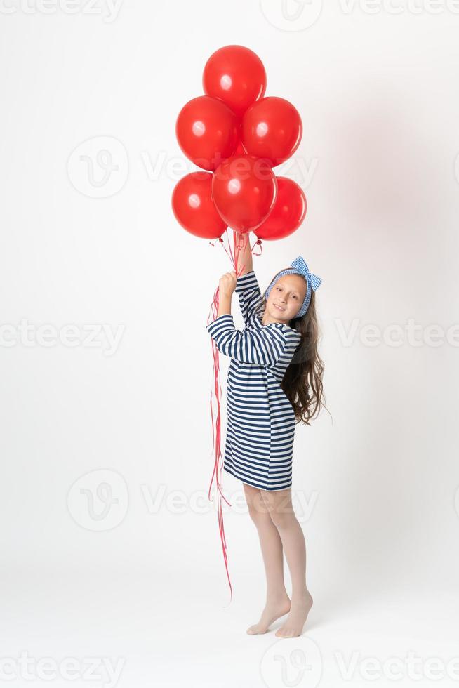 niña participación grande manojo rojo globos en manos, sonriente y mirando a cámara en blanco antecedentes foto