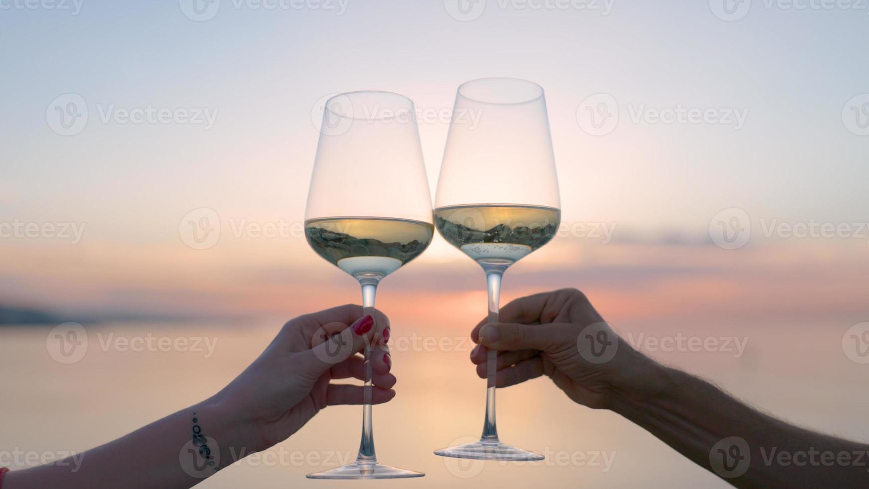 Two hands making a cheers with wine glass against sparkling sea and sky at sunset photo