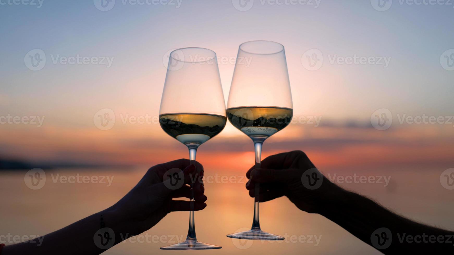 Two hands making a cheers with wine glass against sparkling sea and sky at sunset photo