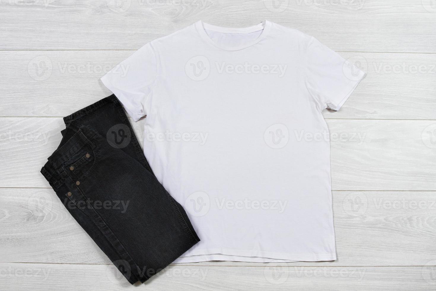 Closeup template blank white t shirt on wooden background. Top view, copy space summer t-shirt casual outfit. Black jeans. Front empty place for print and advertising photo