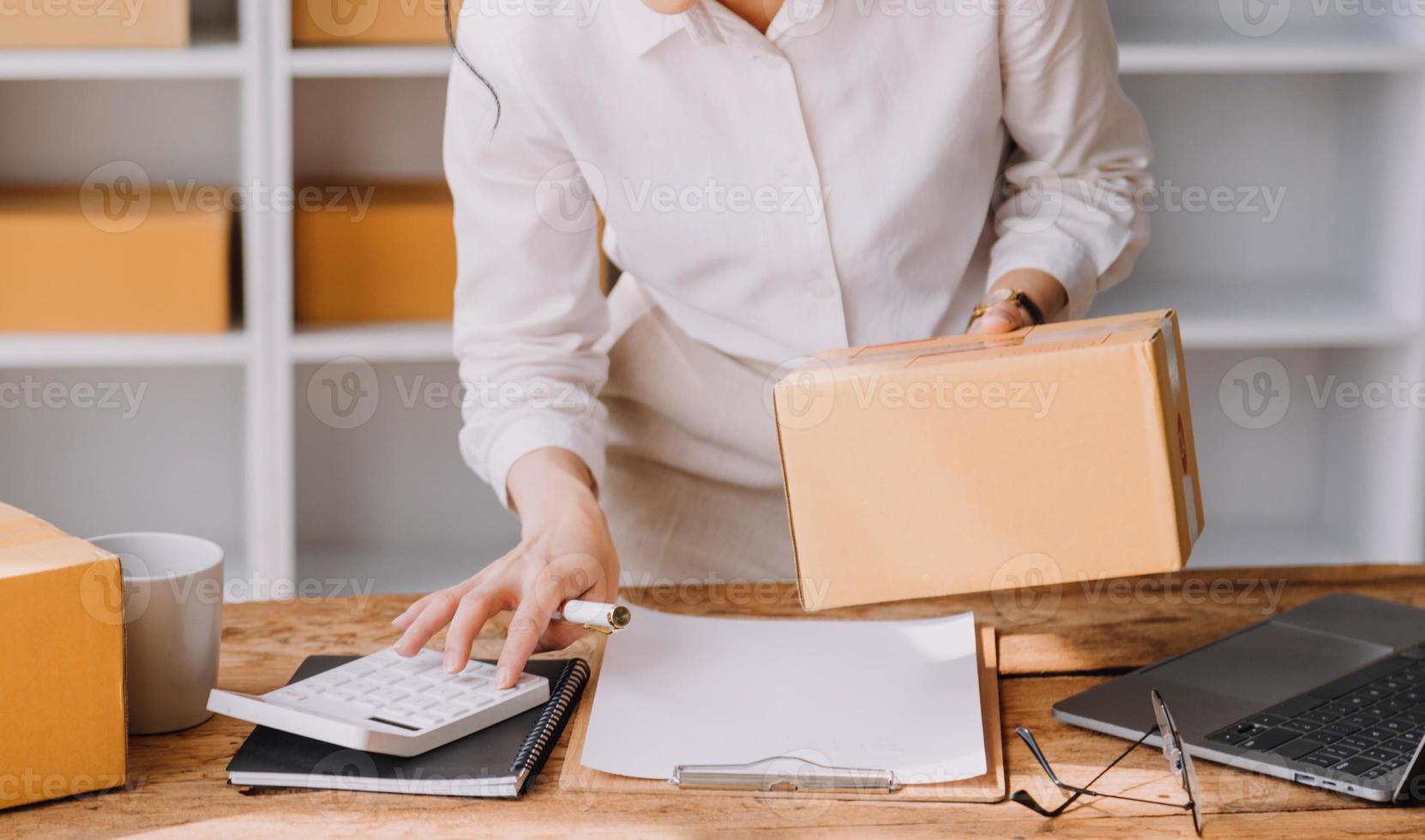 empresaria de pequeñas empresas de nueva creación de una mujer asiática independiente que usa una computadora portátil con una caja de éxito alegre mujer asiática su mano levanta la caja de embalaje de marketing en línea y el concepto de idea de sme de entrega foto