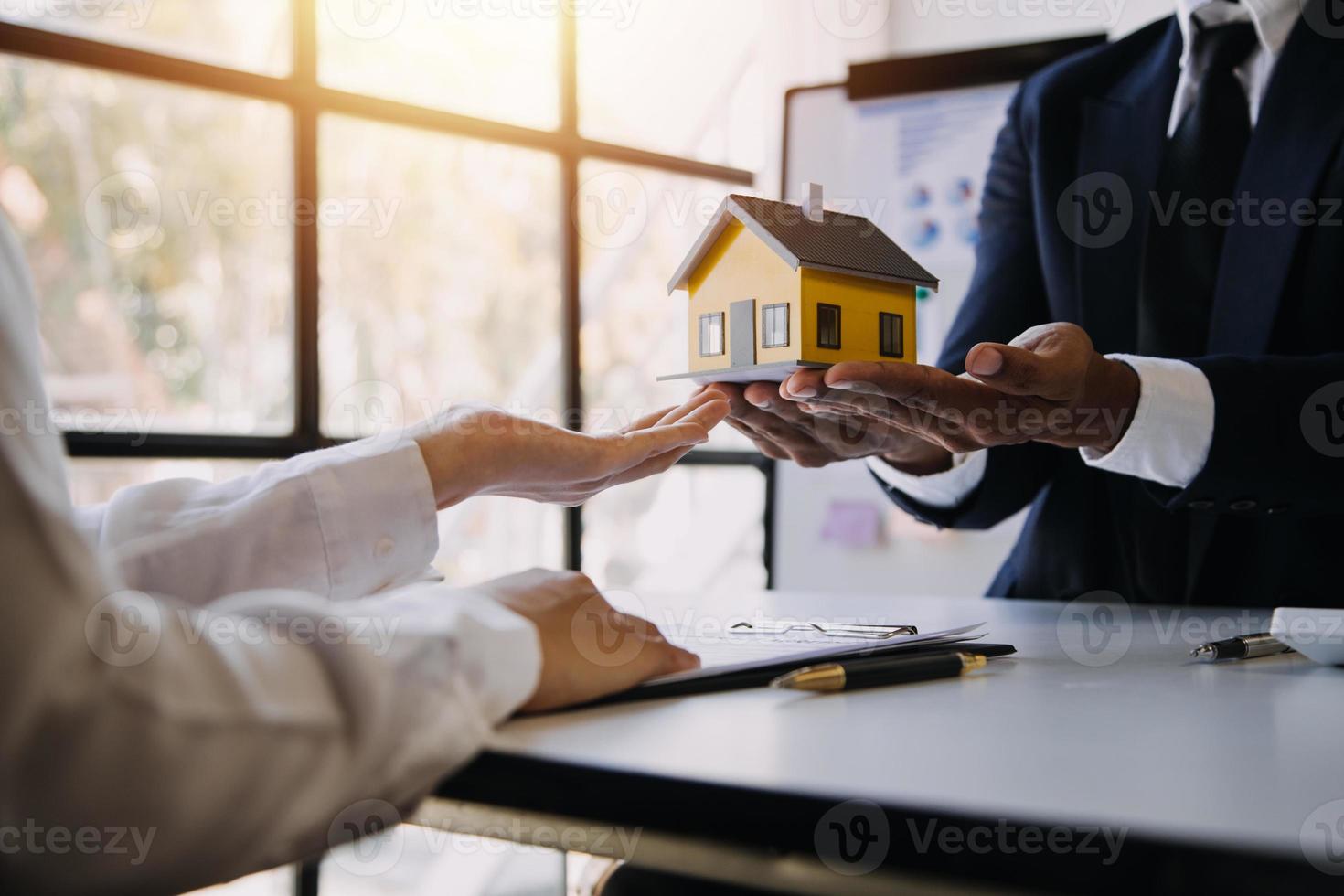 modelo de casa con agente de bienes raíces y cliente discutiendo por contrato para comprar casa, seguro o fondo de préstamo de bienes raíces. foto