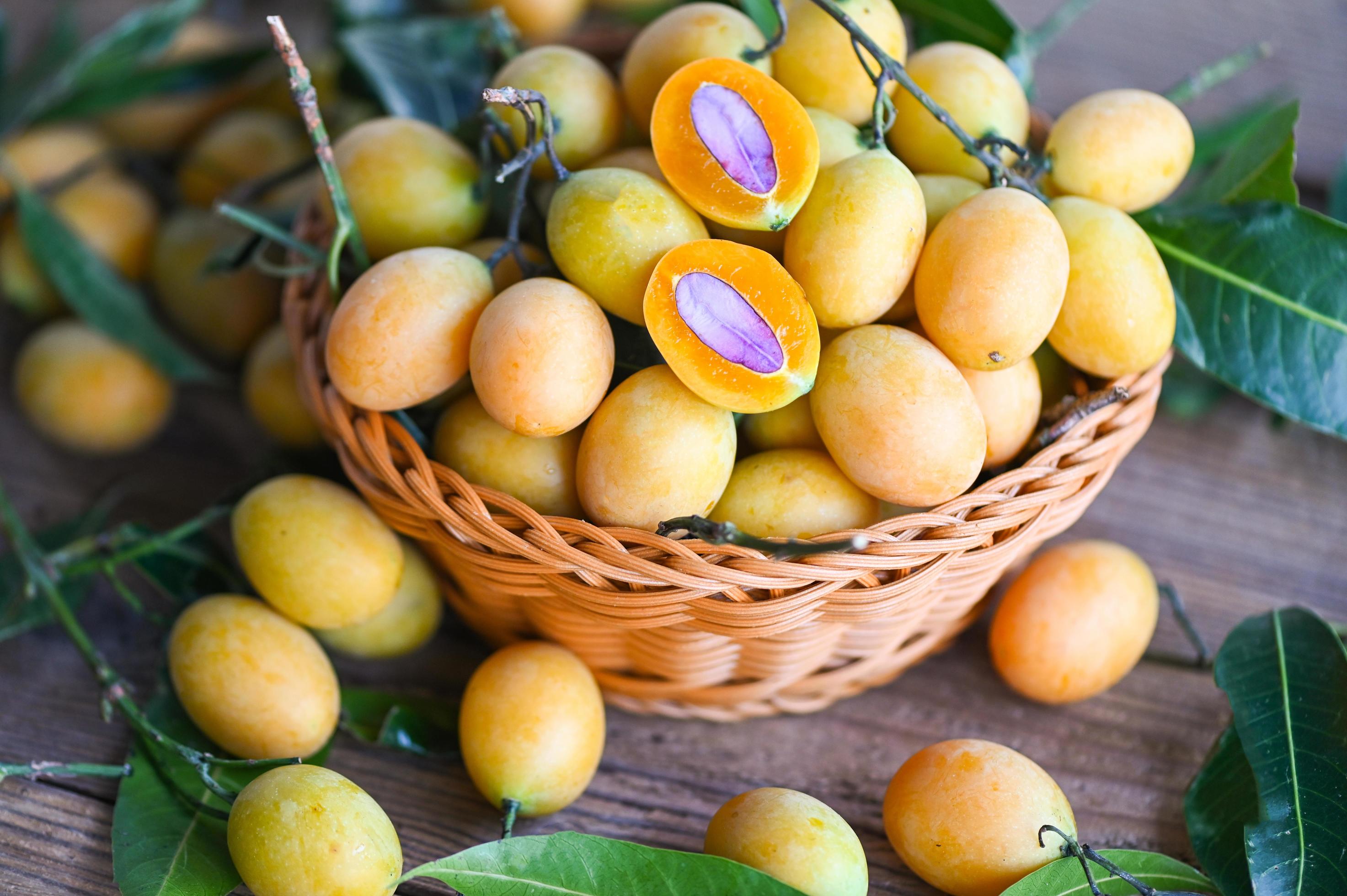 Marian plum fruit and leaves in basket on wooden background, tropical