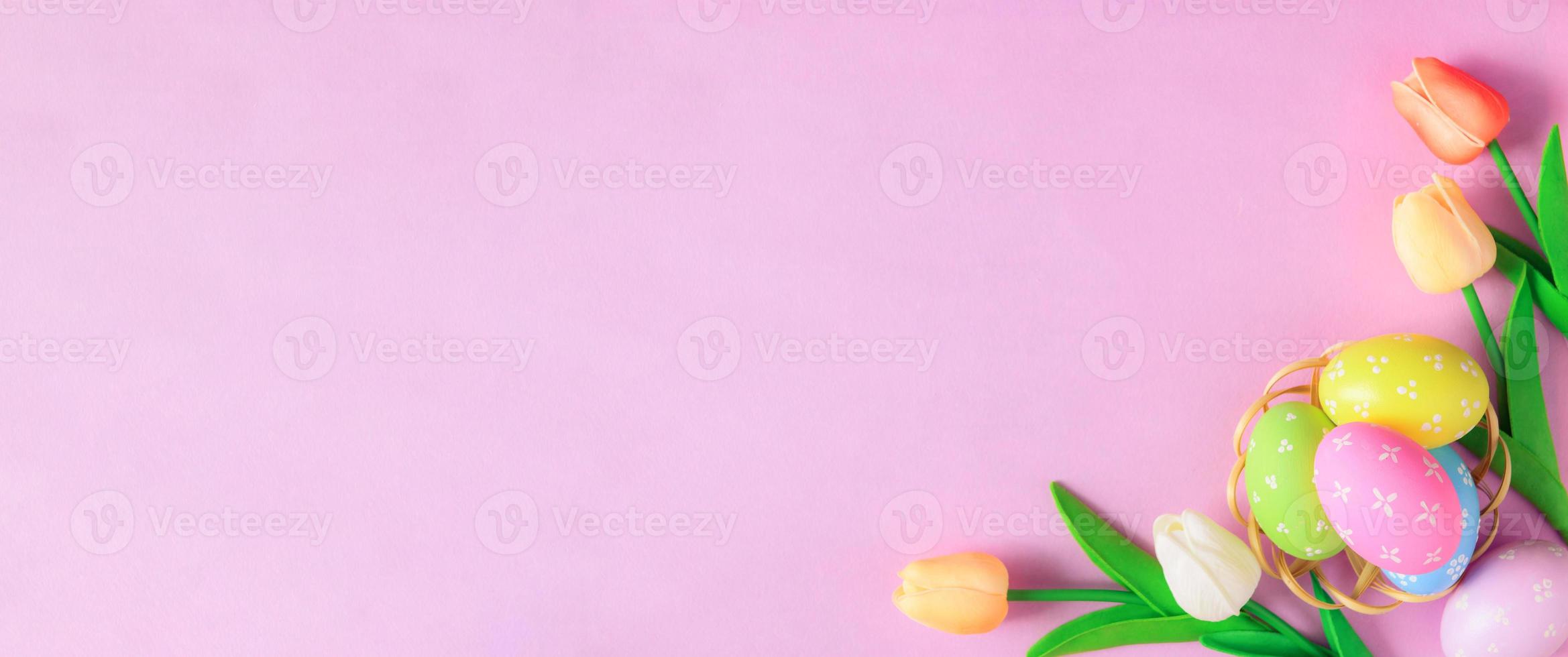 Happy Easter holiday greeting card concept. Colorful Easter Eggs and spring flowers on pastel pink background. Flat lay, top view, copy space. photo
