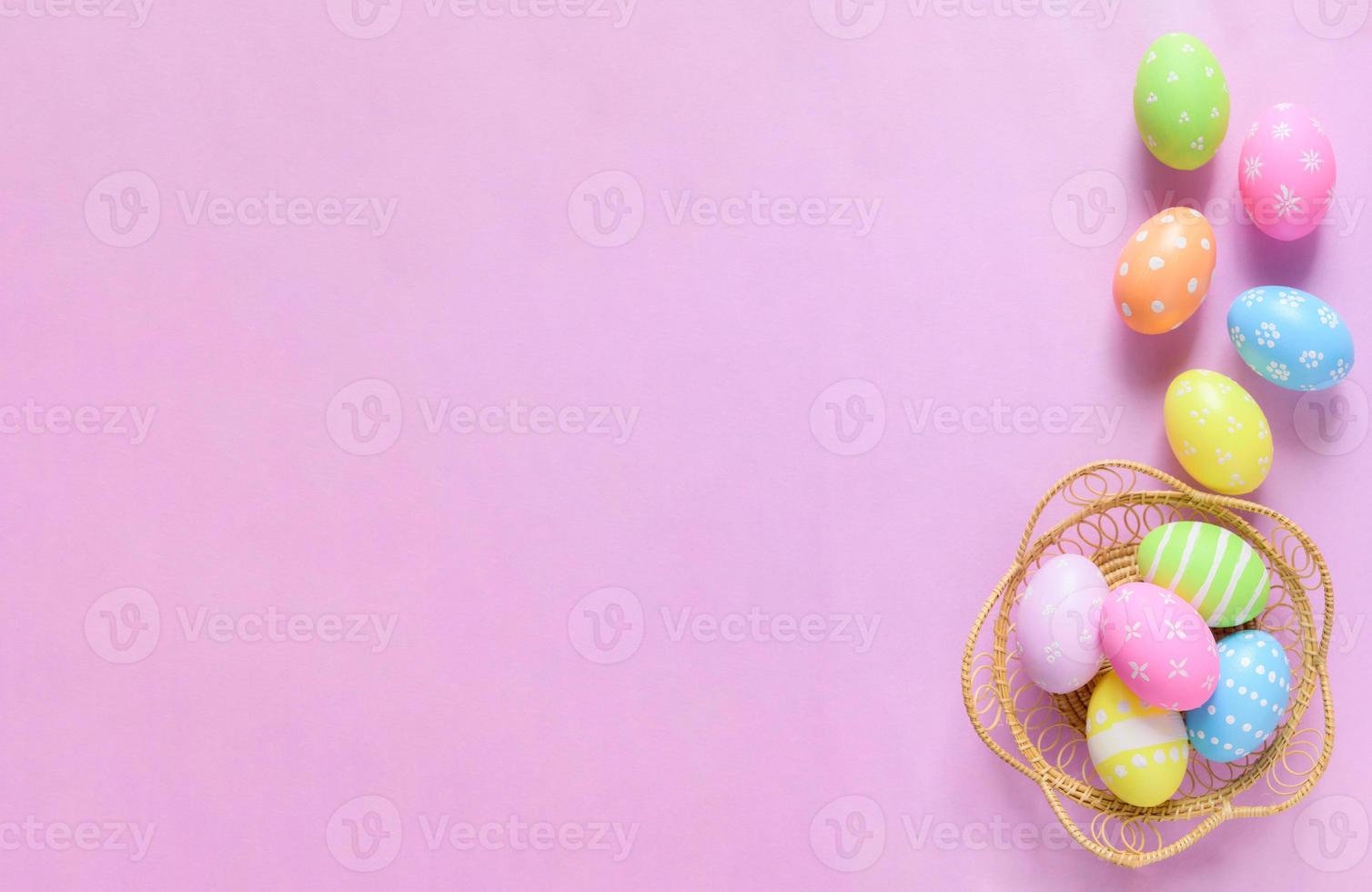 Happy Easter holiday greeting card concept. Colorful Easter Eggs and spring flowers on pastel pink background. Flat lay, top view, copy space. photo