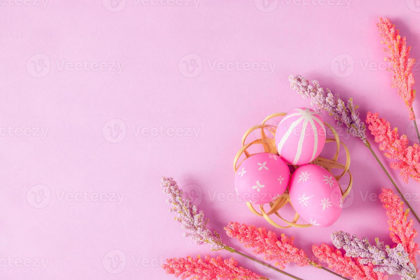Happy Easter holiday greeting card concept. Colorful Easter Eggs and spring flowers on pastel pink background. Flat lay, top view, copy space. photo