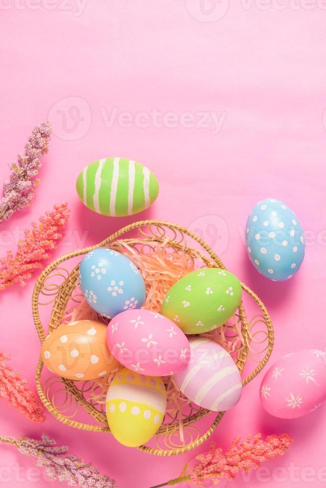 Happy Easter holiday greeting card concept. Colorful Easter Eggs and spring flowers on pastel pink background. Flat lay, top view, copy space. photo