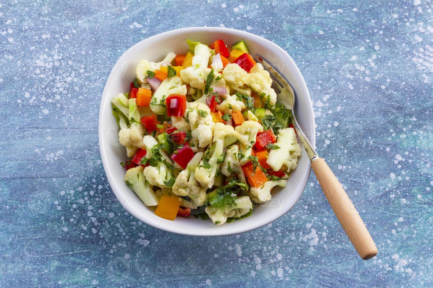 Ensalada de coliflor saludable en tazón blanco sobre fondo de madera azul. foto