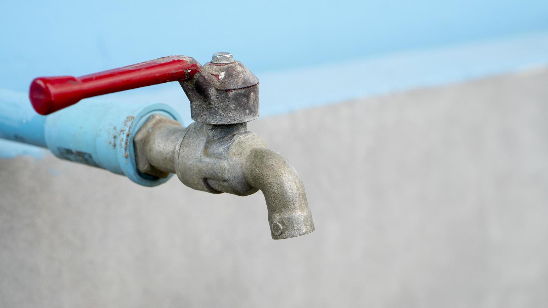 An old faucet with a red handle. And connect from the blue PVC pipe. For use outside the building. photo