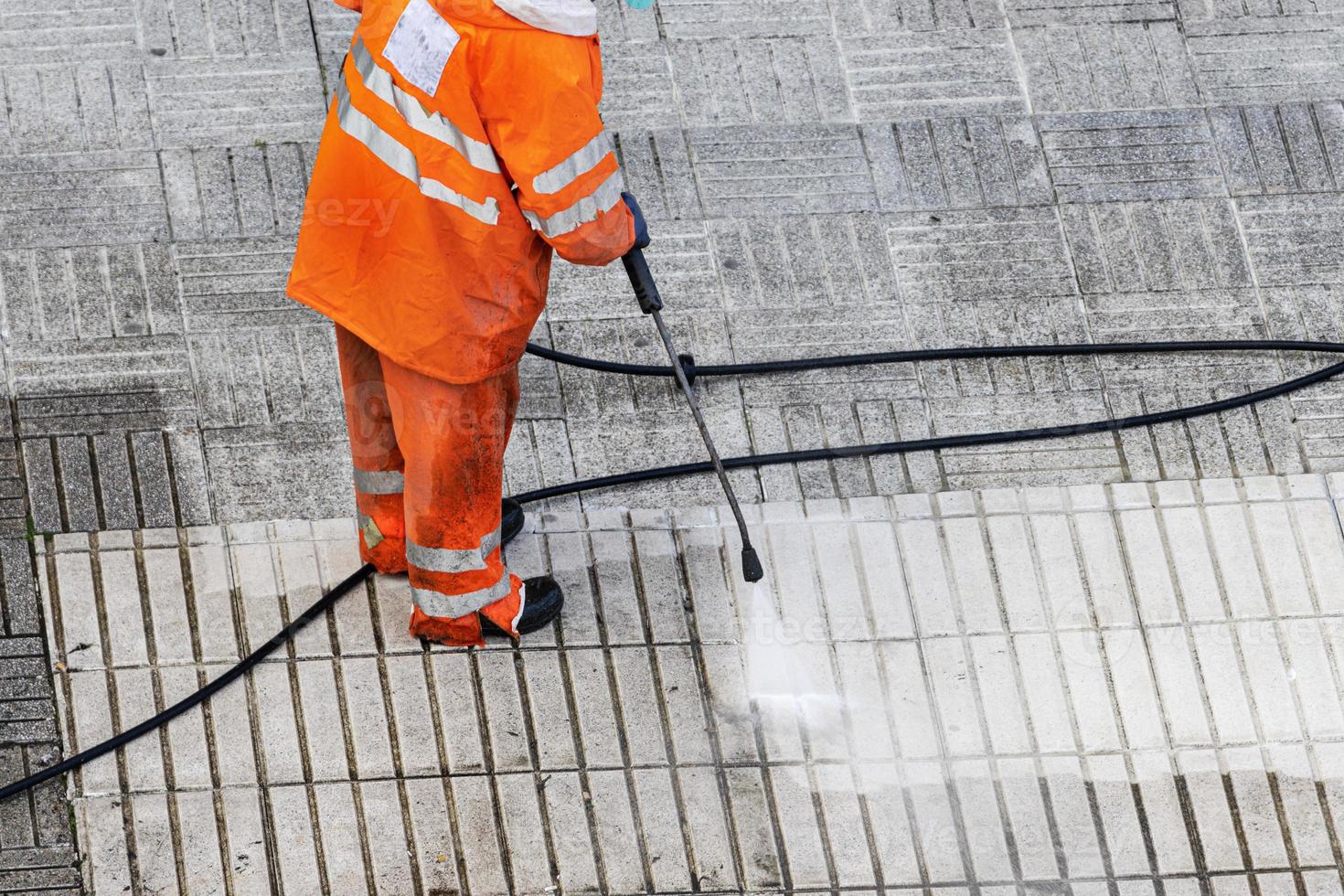 Worker cleaning a street sidewalk with high pressure water jet. Copy space photo