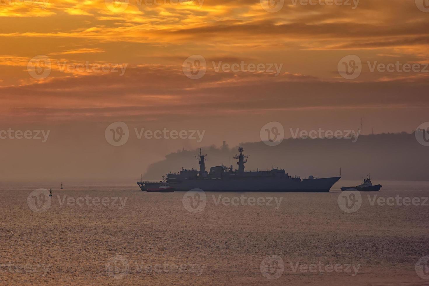 Military Battleship using tugs go to the port at the sunrise time photo