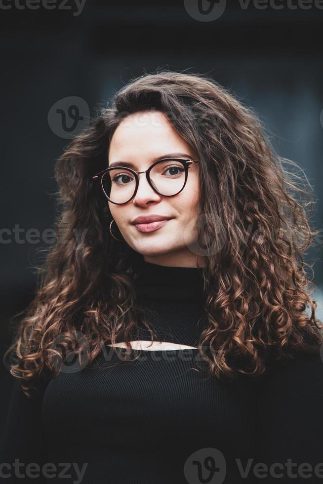 Beautiful young woman with brunette curly hair, portrait in eye glasses enjoying the sun in the city. photo