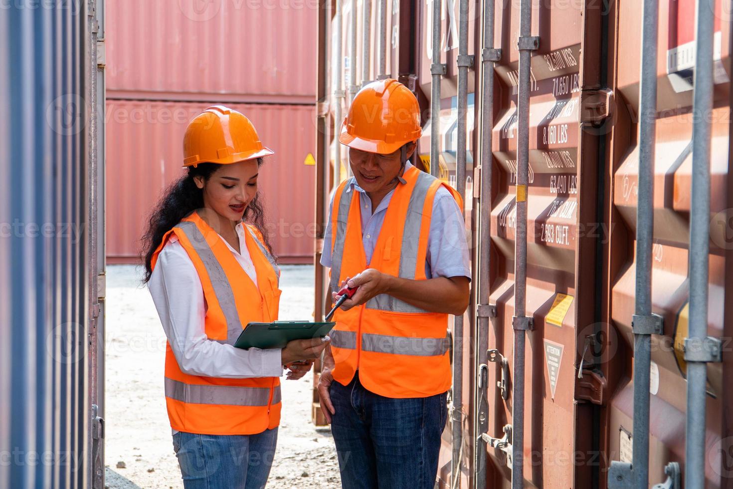 asiático mujer ingeniero con Nota portapapeles y asiático hombre supervisor en difícil sombreros y la seguridad chalecos estar en envase Terminal. envase en exportar y importar negocio y logística. foto