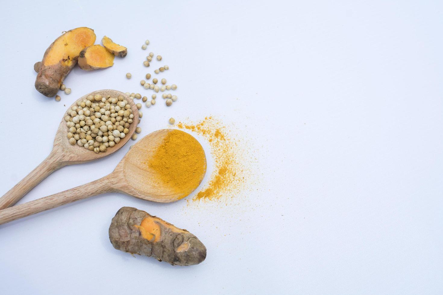 close up dried coriander seeds and turmeric powder in the wooden spoon, isolated on white. raw herbs and spices, negative spaces photo