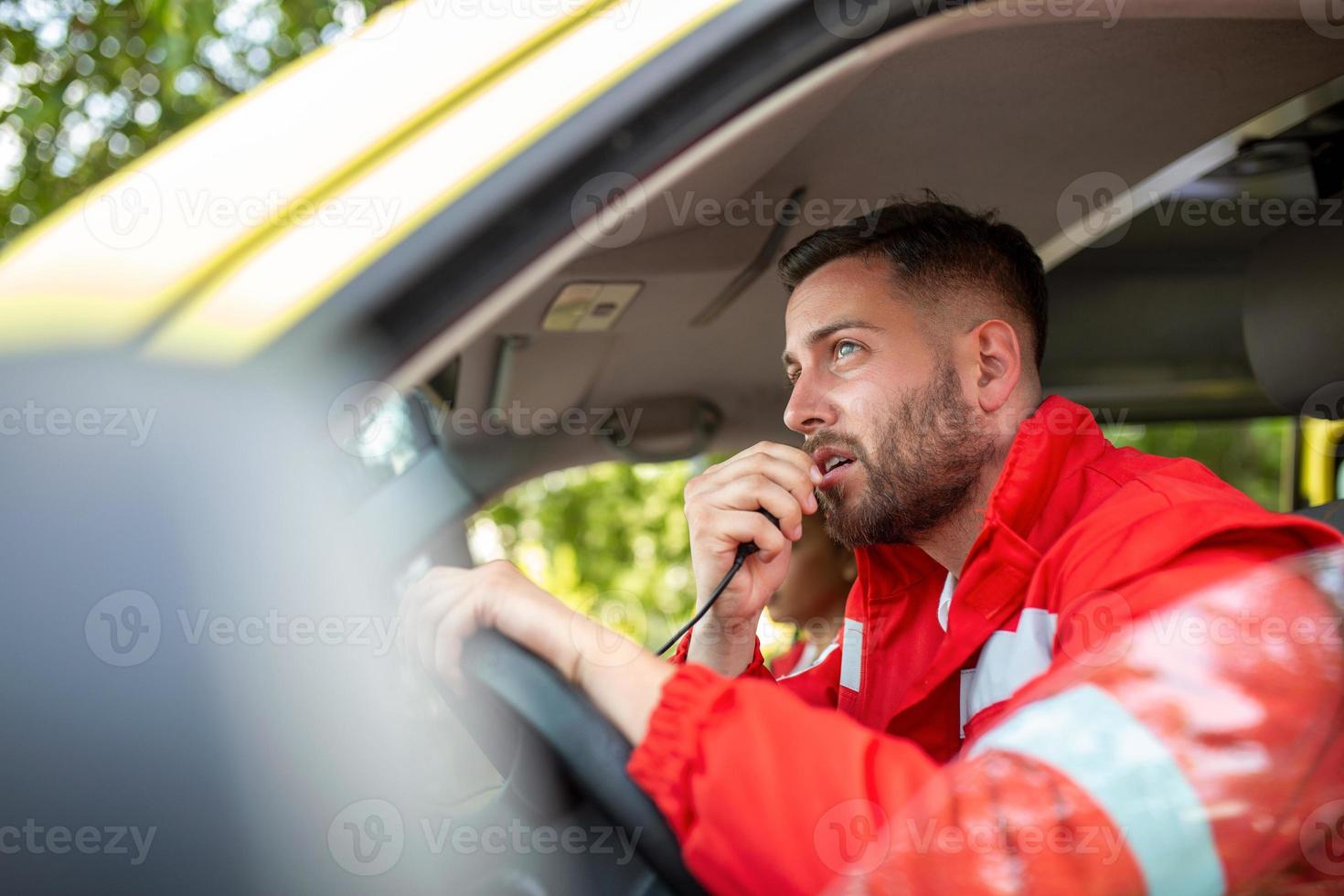 Urgent situation. Two young paramedics in ambulance. Male, caucasian paramedic driving and talking over the radio photo