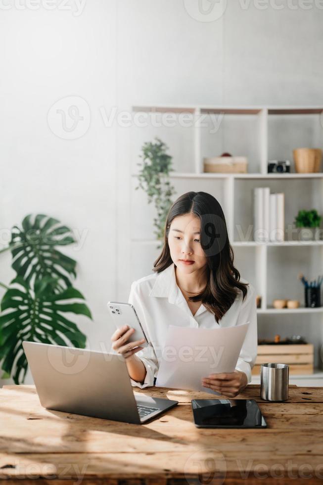 hermosa asiático negocio mujer mecanografía ordenador portátil y tableta metido a el mesa a hogar oficina foto