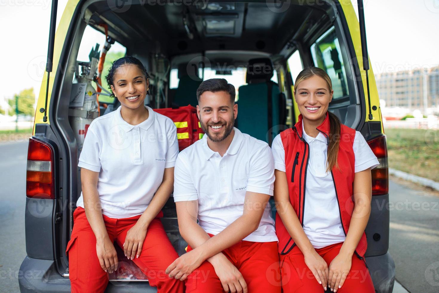 paramédicos y médico en pie a posterior de ambulancia. médico es que lleva un médico trauma bolsa. grupo de Tres paramédicos en pie en frente de ambulancia con sonrisa. foto