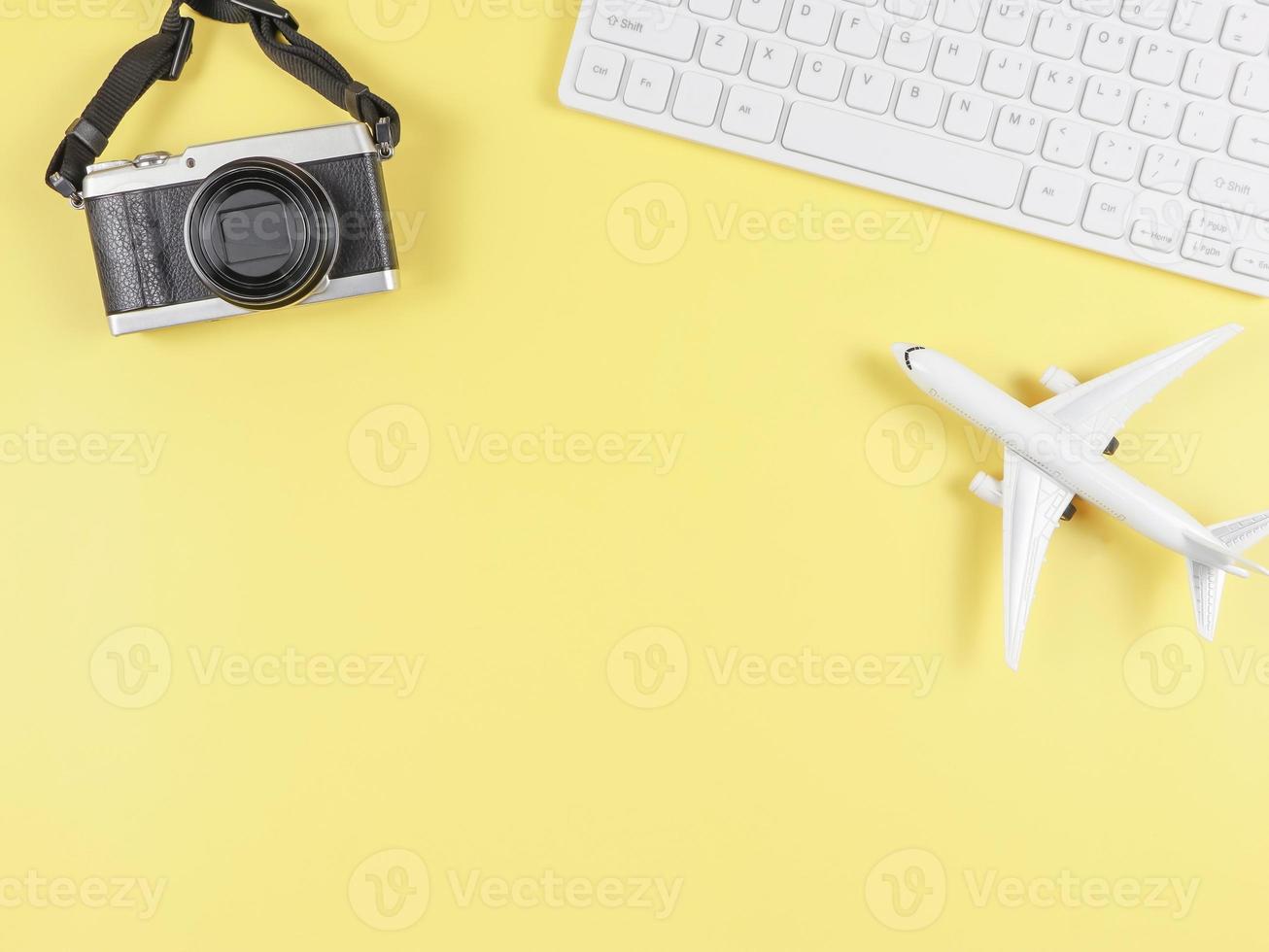 flat lay of airplane model, computer keyboard, and digital camera with copy space on yellow background, business and traveling concept. photo