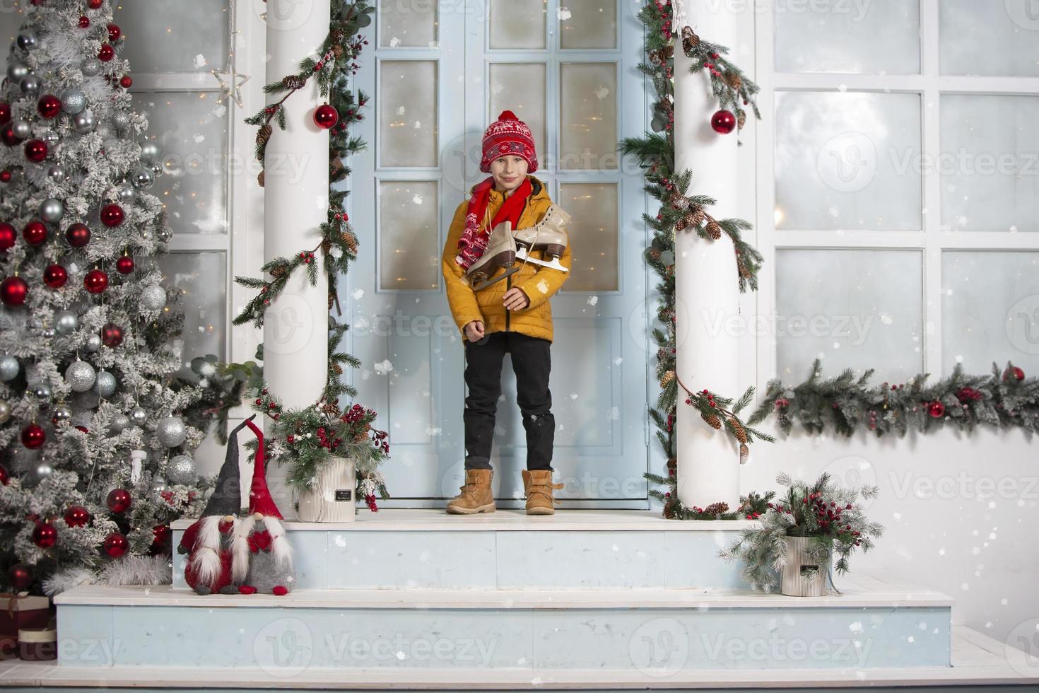 Handsome little boy in christmas. Funny child holds old skates and stands on the porch of a house decorated with Christmas tree decorations photo