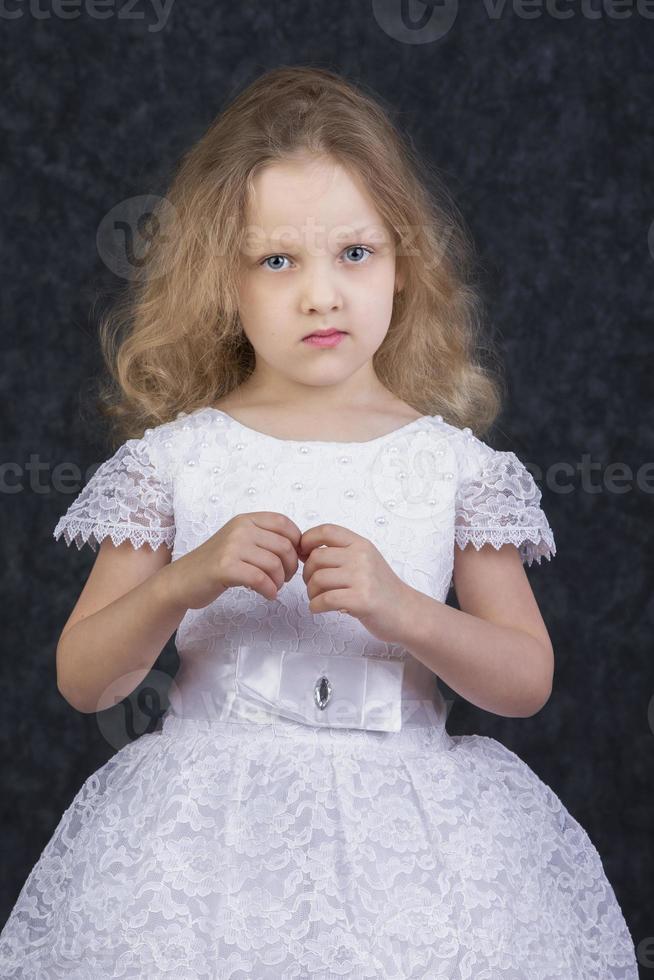 linda pequeño rubia niña en un hermosa blanco vestir en un oscuro antecedentes. seis año antiguo hermosa niña foto