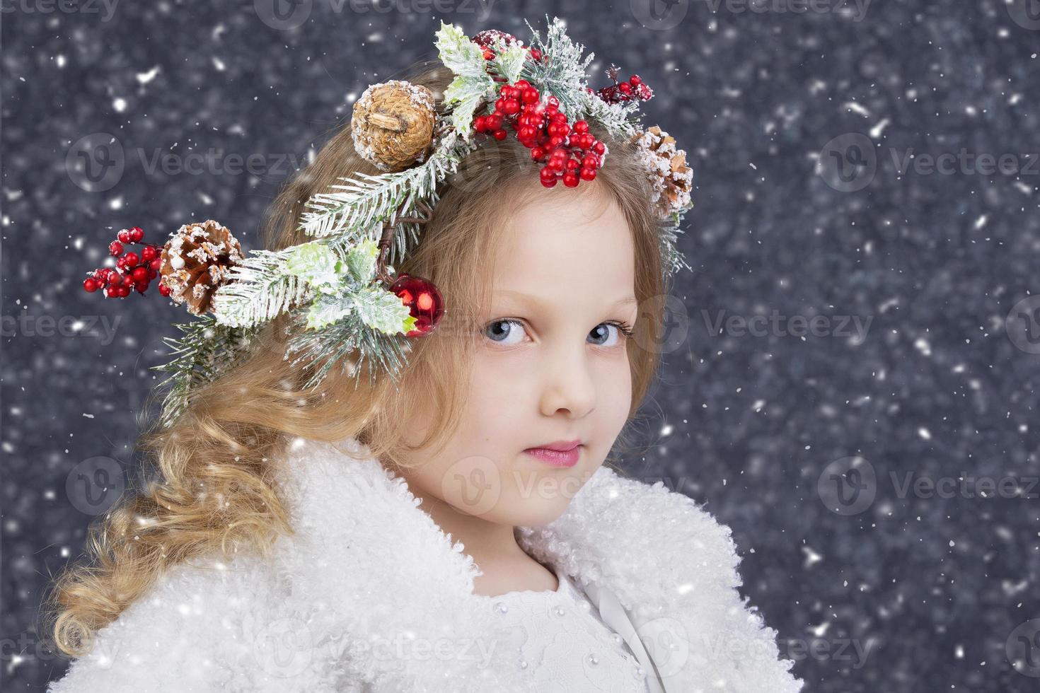 Beautiful little blonde girl with a Christmas wreath on her head on a gray background with falling snow. Christmas child. photo