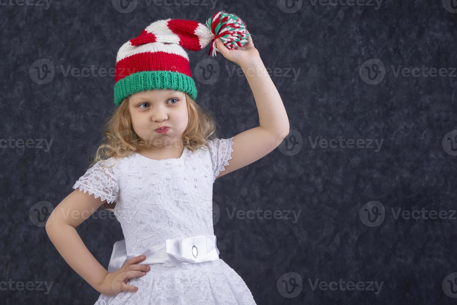 Funny little blonde in a knitted Christmas hat with a pompom. Happy beautiful child about five years old. photo